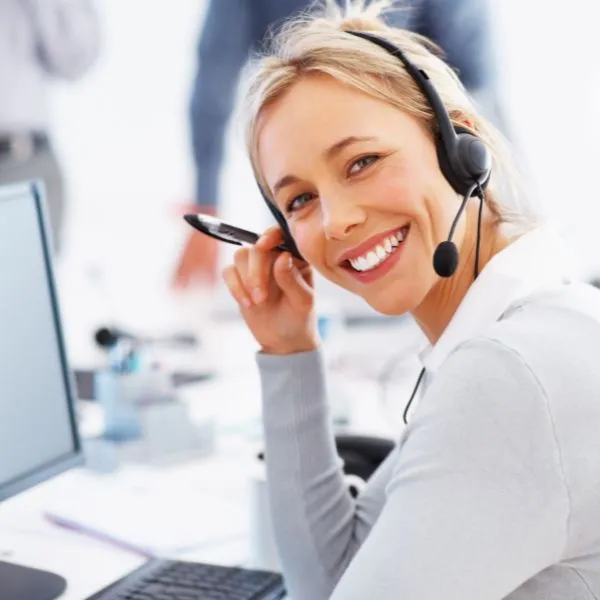 A friendly, smiling customer support professional wearing a headset in a bright, modern office environment.