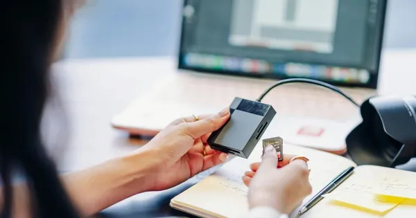 A close-up of hands inserting an SD card into a reader next to a laptop. Protect your small business from unexpected data breaches today.