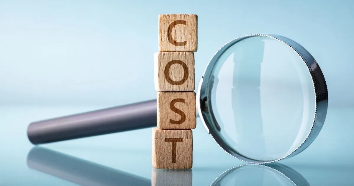 Explore the impact of hidden expenses with this visual of a magnifying glass examining the word COST on wooden blocks
