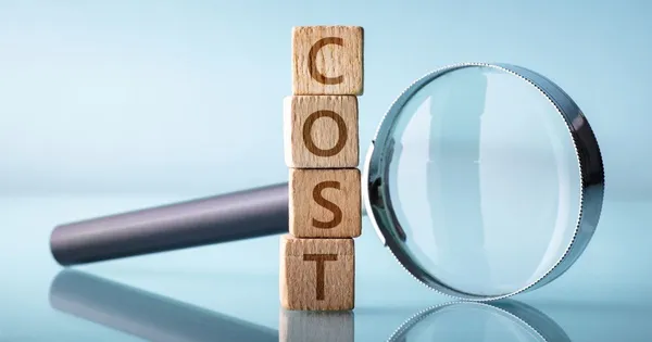 Explore the impact of hidden expenses with this visual of a magnifying glass examining the word COST on wooden blocks