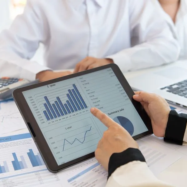 A professional business advisor and entrepreneur reviewing a digital dashboard on a tablet. The screen displays "1 Year" performance charts, including bar graphs and line trends, indicating upward growth and sales summaries.